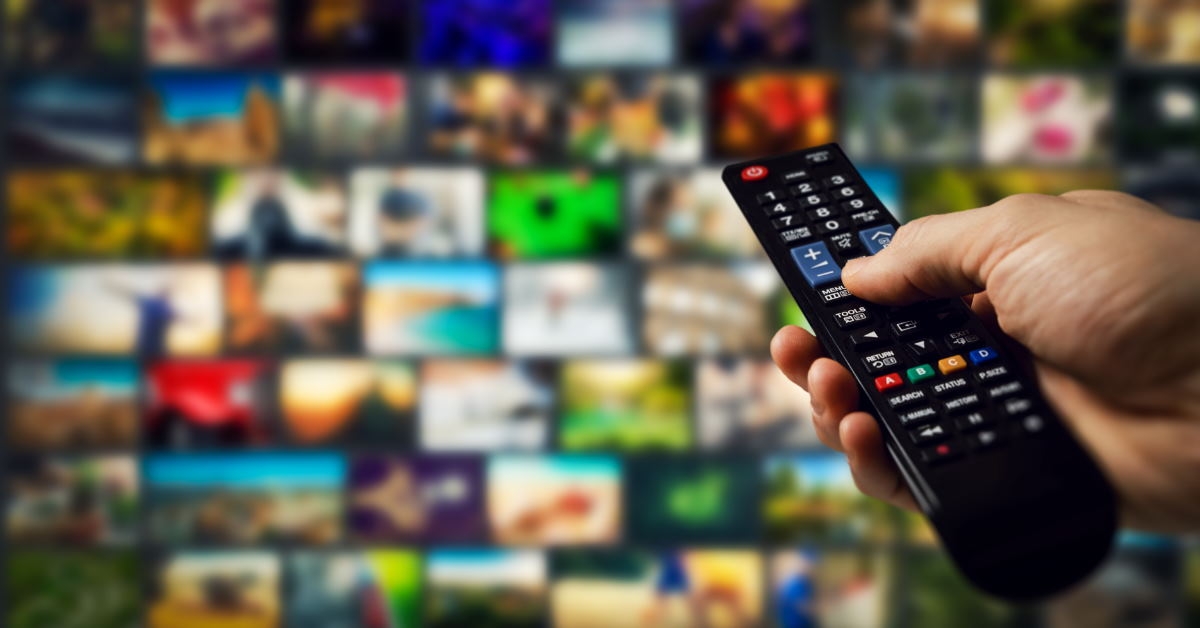 hand holding tv remote at smart tv with programs in background