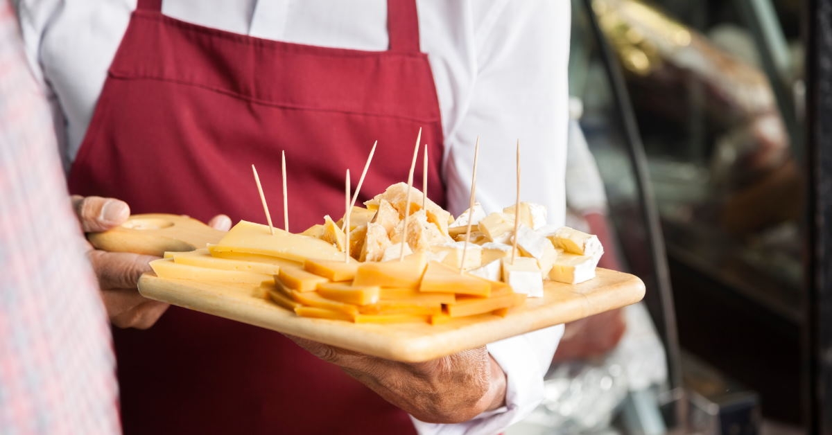 salesman in grocery store holding wooden cutting board with various type of cheese slices