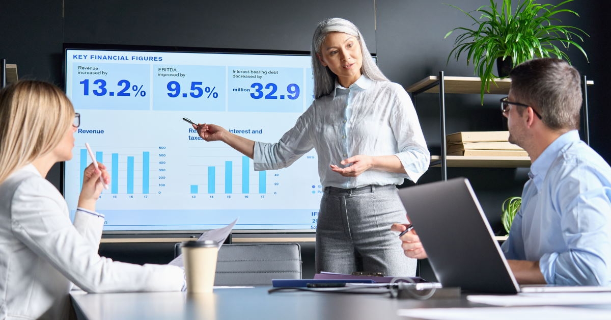 senior woman standing in meeting room explaining data on projector to colleagues