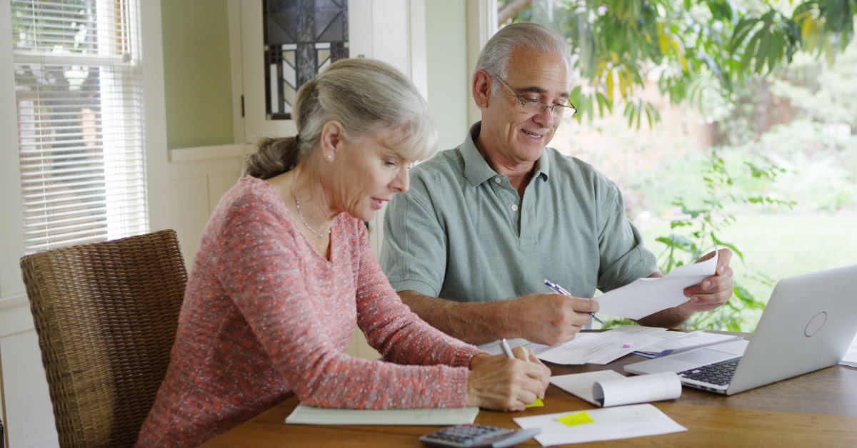 senior couple sitting at table calculating and paying bills using laptop