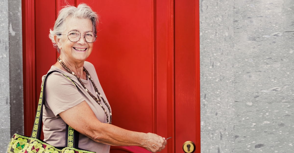 senior woman smiling for photo carrying handbag opening door using key