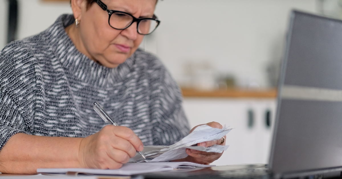 senior woman sitting at table reviewing tax papers with laptop 
