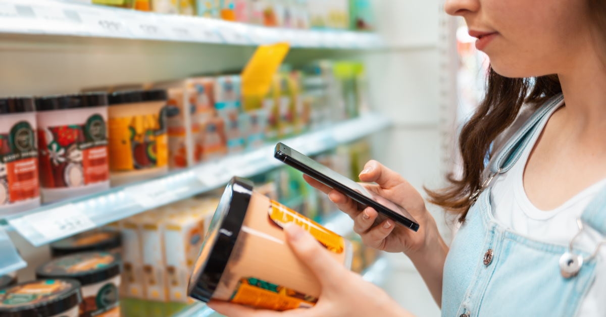 woman standing in store holding body lotion jar checking its composition using smartphone