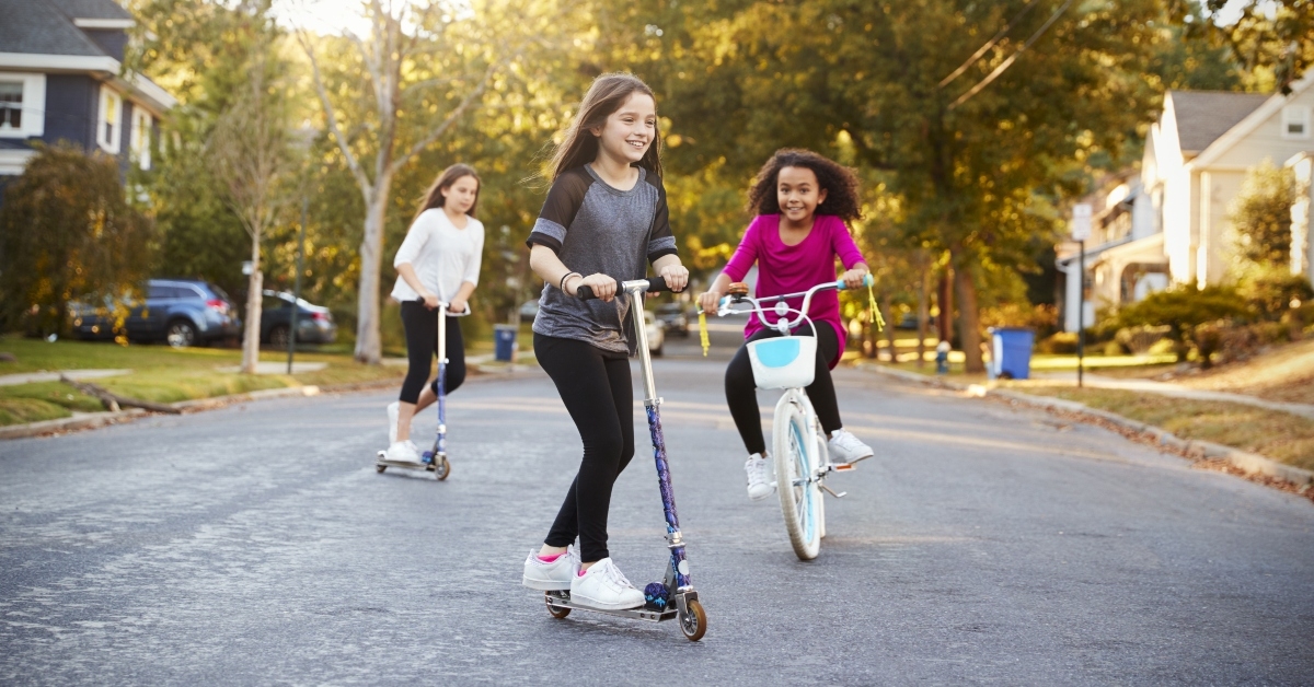 three girls riding down the street on scooters and a bike