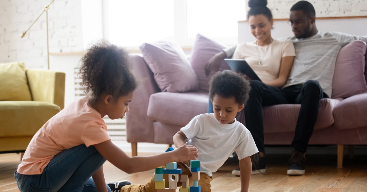 happy couple sitting on couch with children playing with blocks on ground