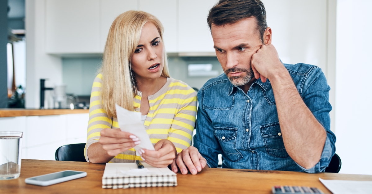 couple sitting on chair in home arguing over taxes with notepad and calculator on table