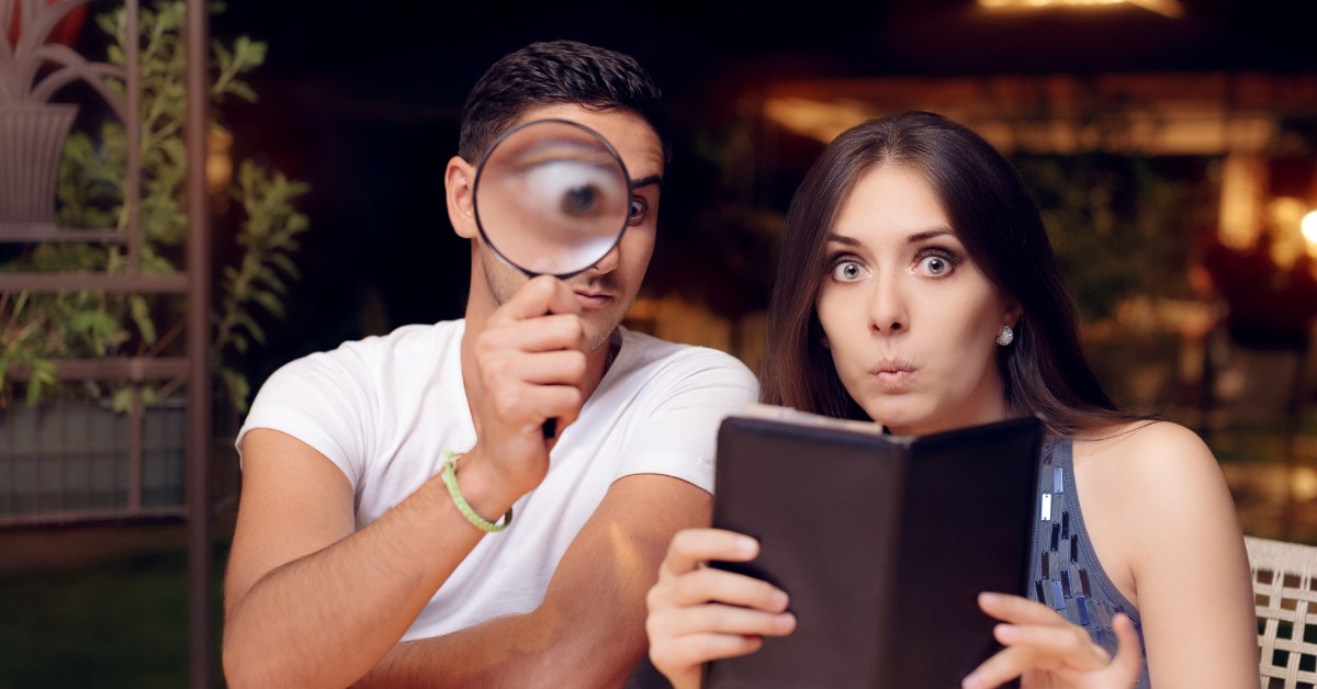 couple sitting in restaurant shocked at bill holding magnifier