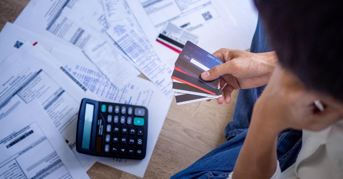 man sitting on ground with credit cards in hand and calculator on papers