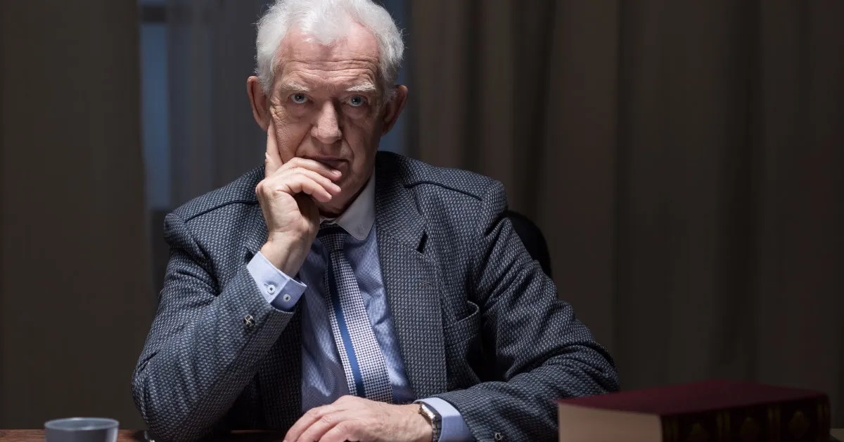 senior businessman sitting at table lost in serious thoughts with hands on face 