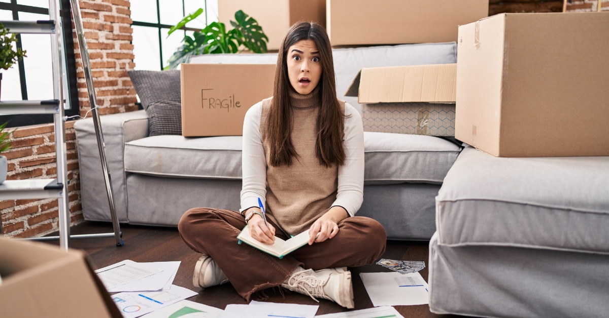 surprised woman sitting on ground writing expenses on notebook
