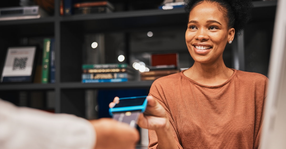 african american woman in store giving card for digital transaction using atm device