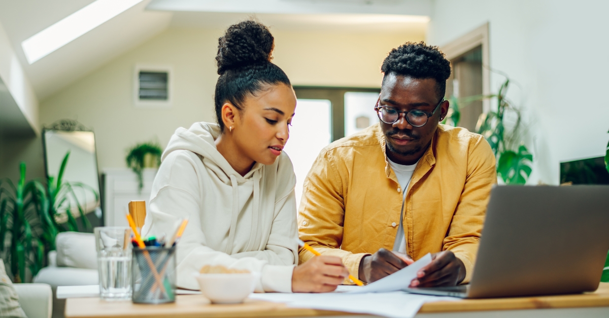 diverse couple using laptop and looking into the blueprints