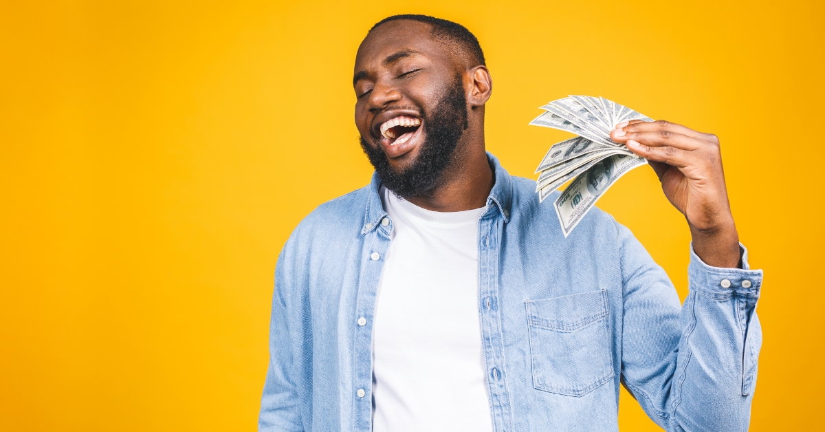 african american man standing in front of yellow wall flaunting money in surprise 