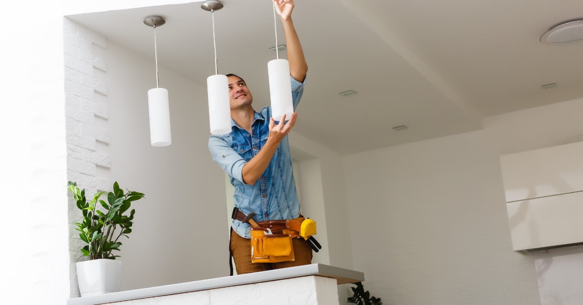 male electrician standing on staircase to install stylish lamps on ceiling at new home