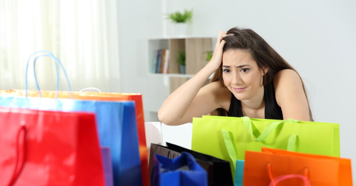 shopaholic woman sitting at home holding head while looking at numerous shopping bags