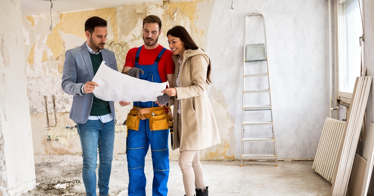 young couple looking blueprints of their home with handyman