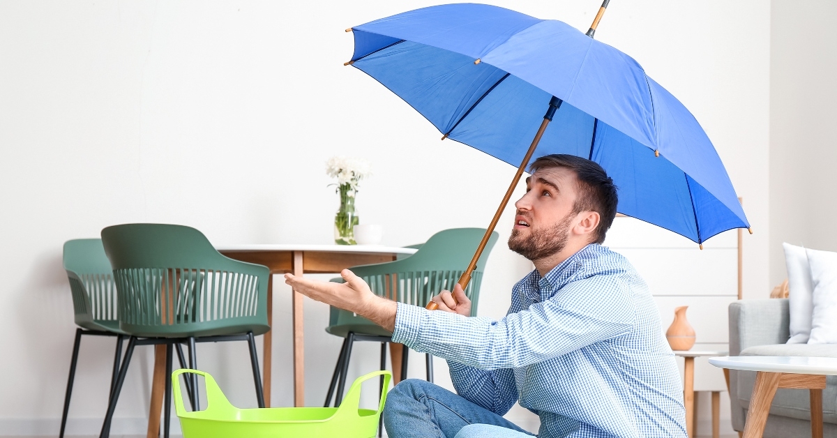 young man with umbrella suffering from neighbors flood at home