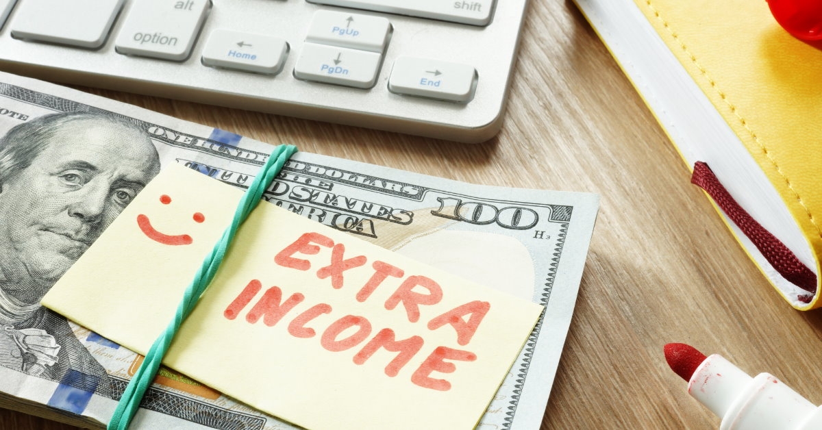 extra income sticky note place on pile of money on table besides keyboard and red marker