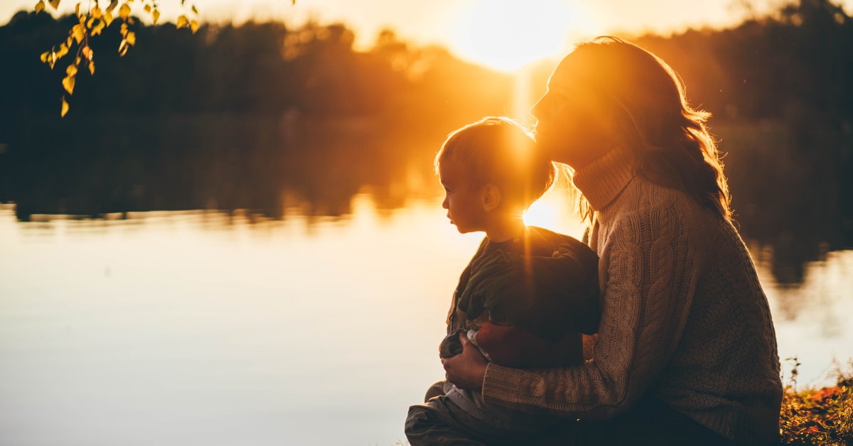 mother and her son are sitting beside the lake, having a good time together