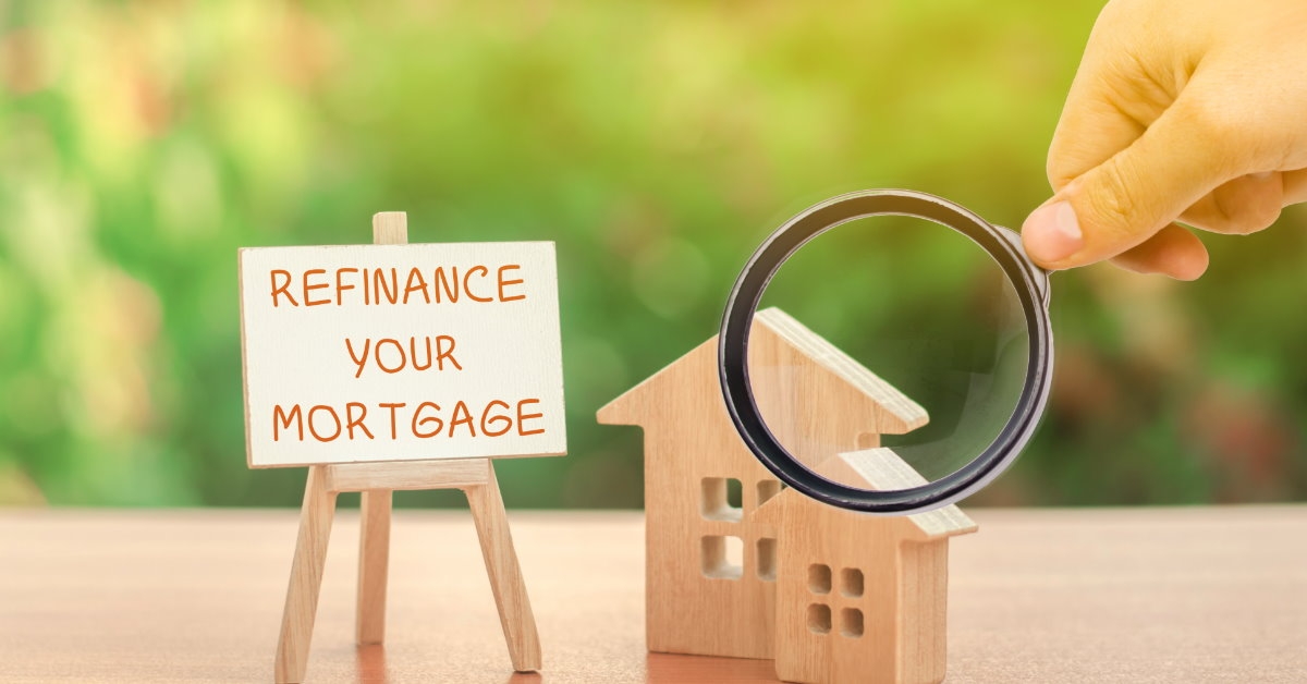 refinance and mortgage sign on miniature canvas besides hand using magnifying glass on house sculpture showing real estate finance concept