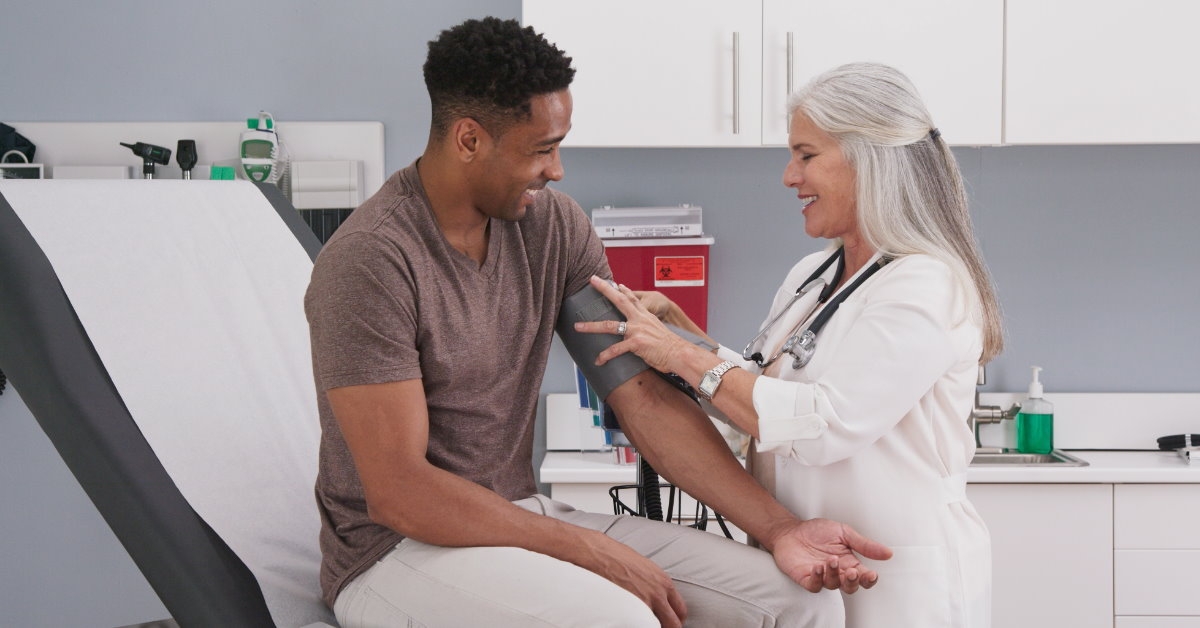 happy african american man sitting on stretcher getting his blood pressure checked by a cheerful senior doctor