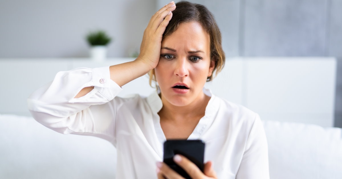 woman holding her head in shock at spam messages on smartphone at home