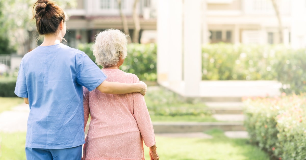 senior woman walking using the support of a female nurse on the lawn outdoors