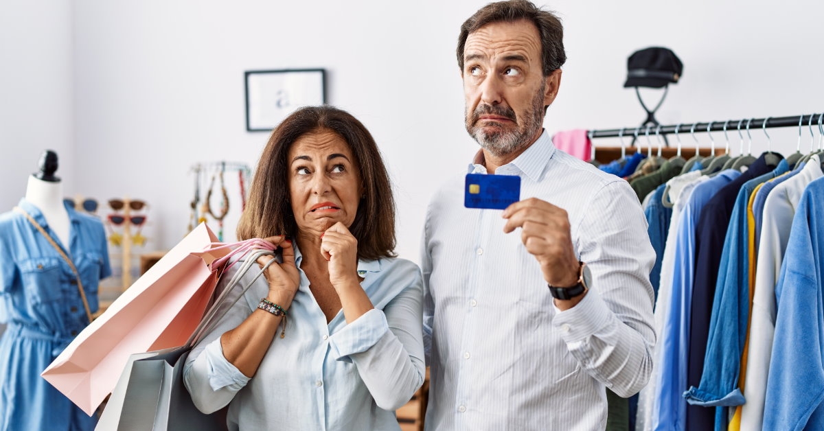 Worried senior couple in retail store holding card and shopping bags