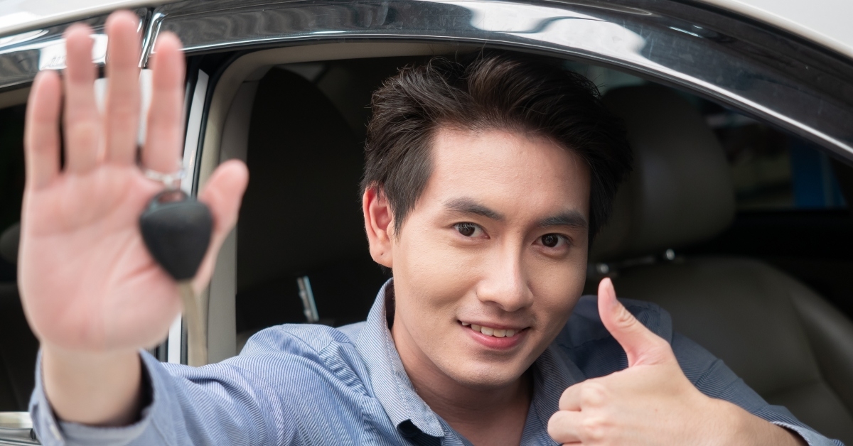 asian man sitting in new car and showing car keys