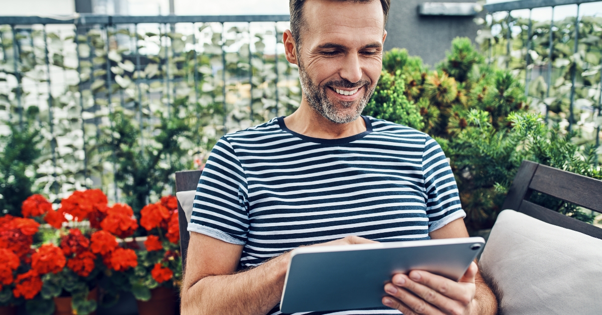 cheerful man sitting relaxed on patio using digital tablet
