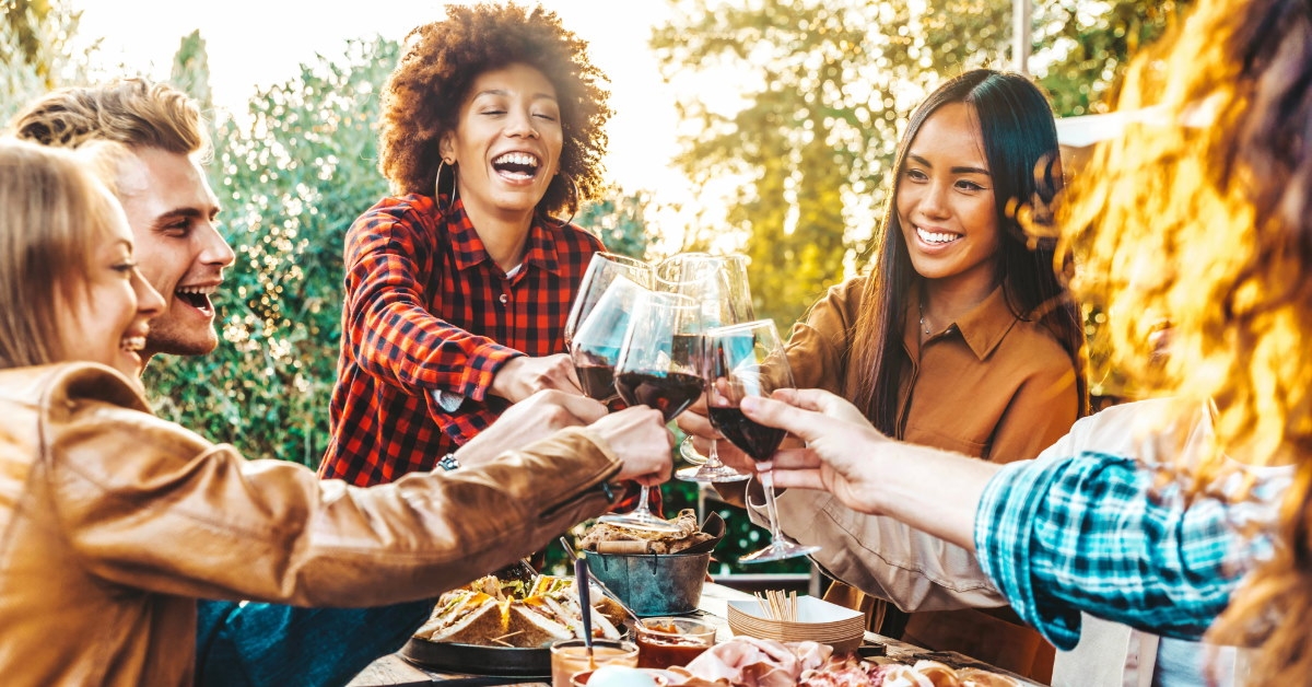 multi ethnic friends at bbq party outdoors doing cheers with their glass of champagne with food on table