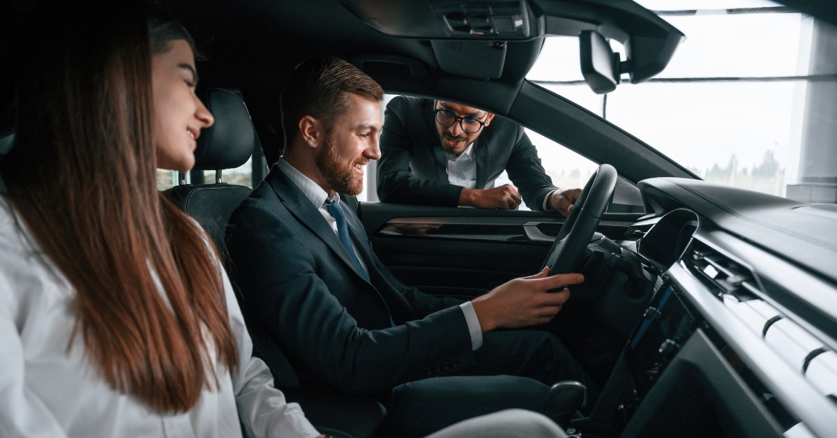 couple sitting inside car in showroom talking with car dealer