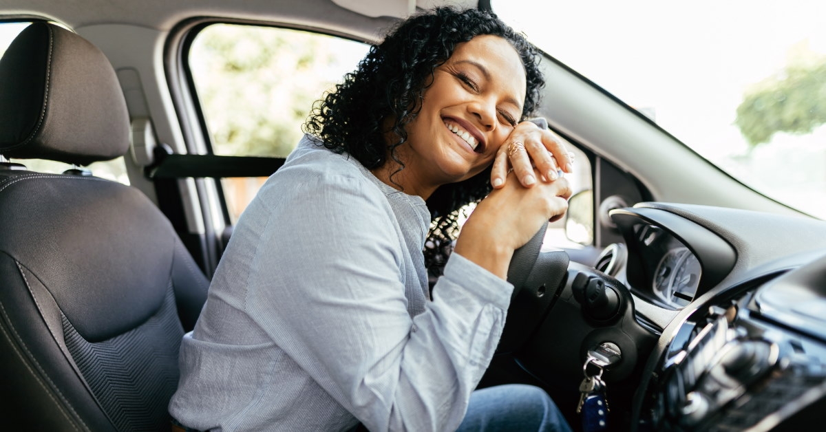 woman sitting at drivier's seat wearing seat belt hugging steering wheel