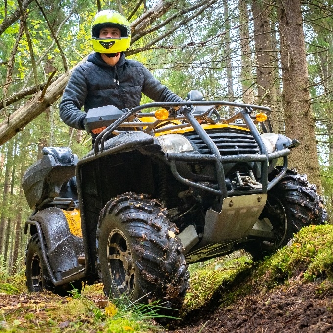 man in a yellow helmet rides a Quad bike through the woods