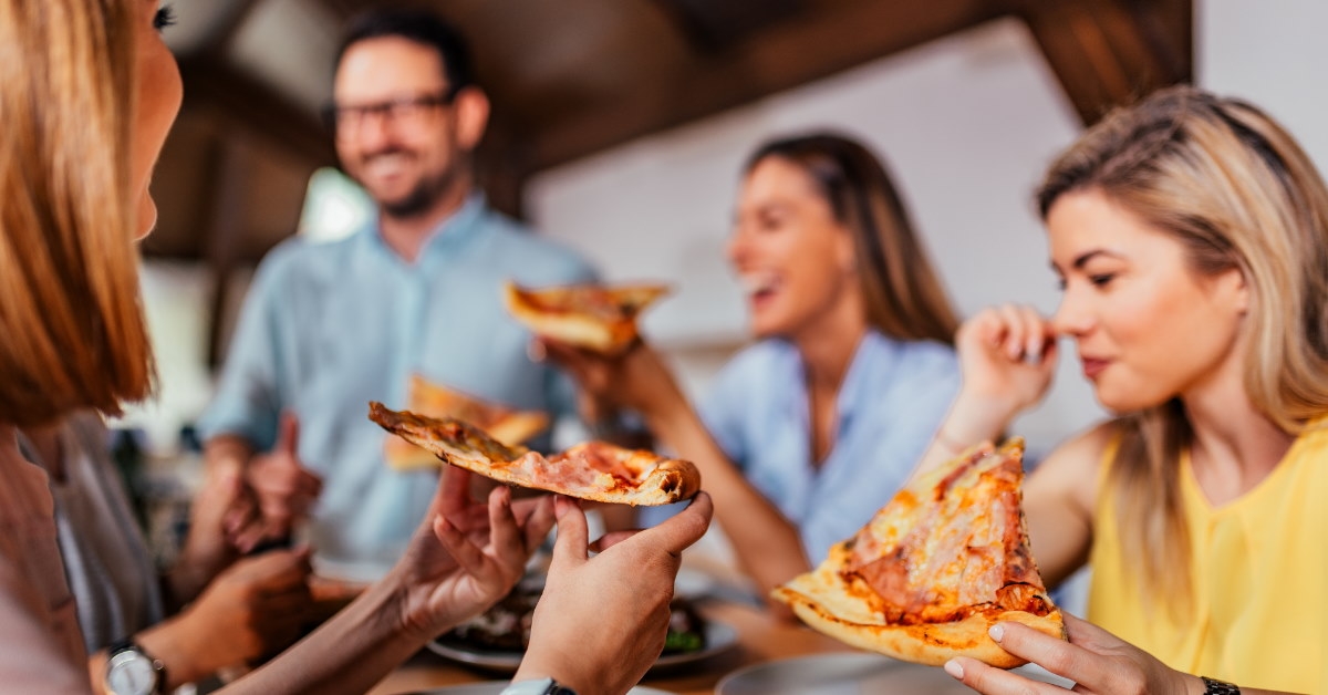 colleagues sitting at wooden table eating pizza 