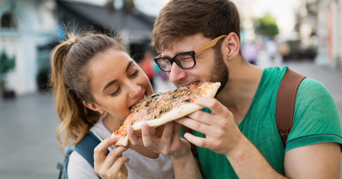 couple enjoying pizza slice together on outdoor street