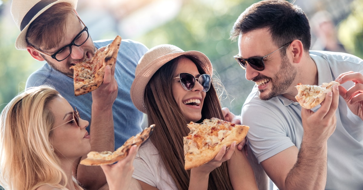 group of friends enjoying pizza outdoors on sunny day