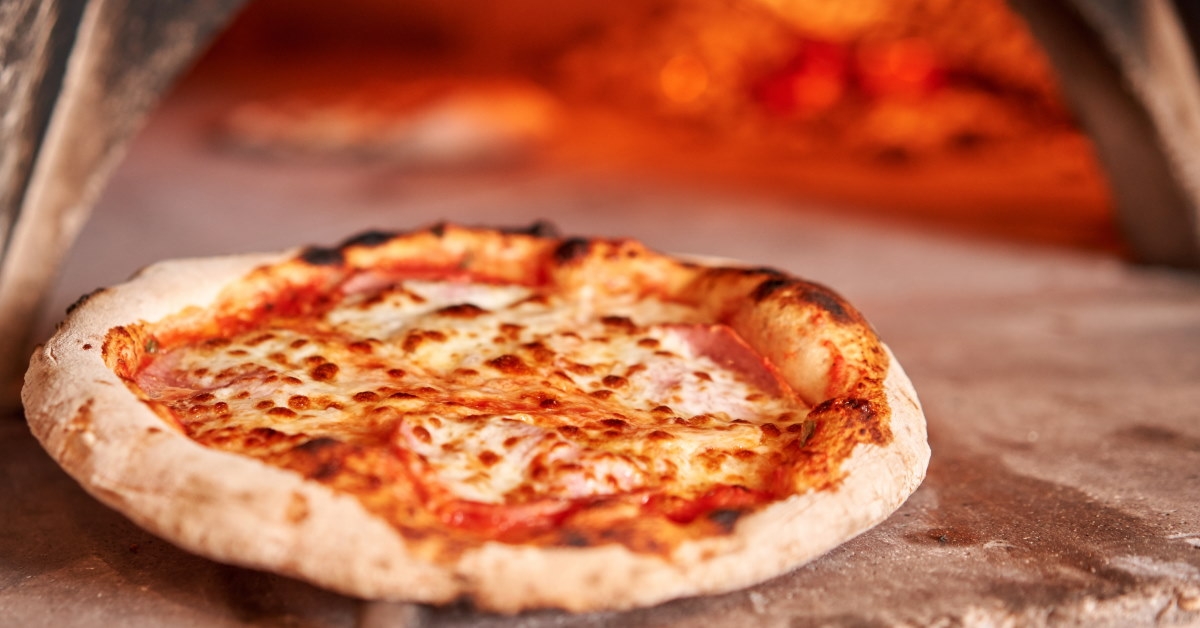 freshly baked margherita pizza placed outside traditional wooden oven