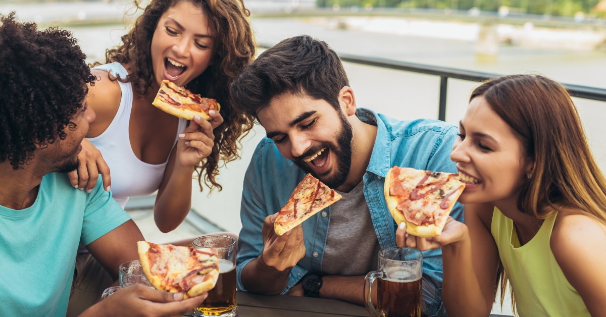 friends sitting at outdoor restaurant enjoying pizza with champagne 