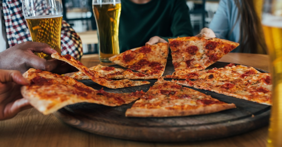 friends sitting at table with champagne glasses having pizza in cafe