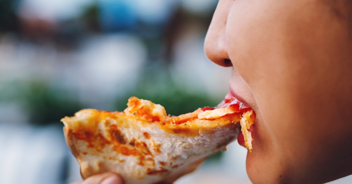 girl eating a slice of delicious pizza at outdoor restaurant