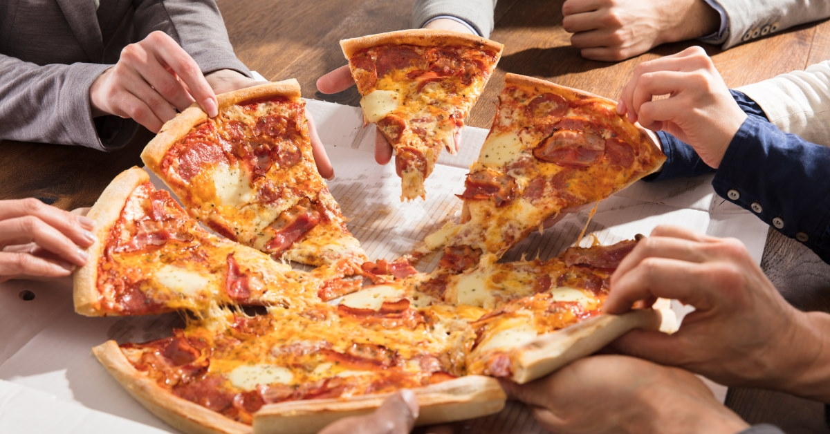 people sitting at wooden table pulling apart pizza slices to eat