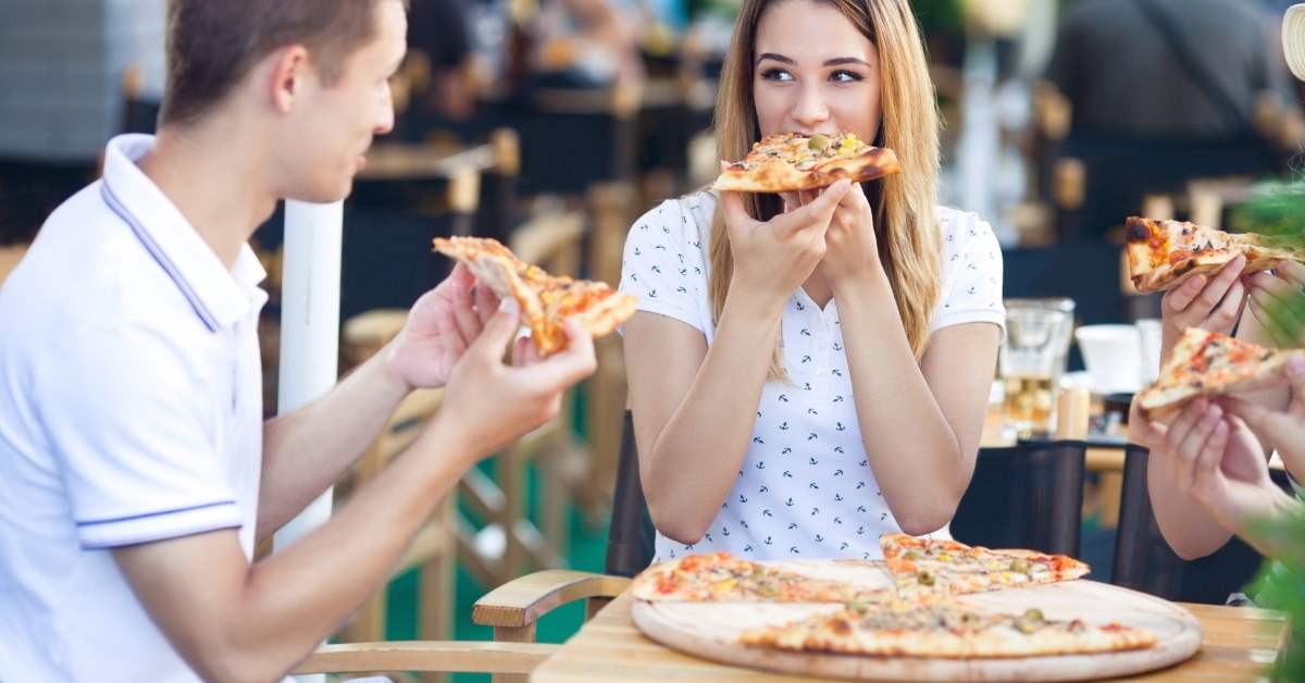 group of young friends sitting in outdoor restaurant eating pizza together 