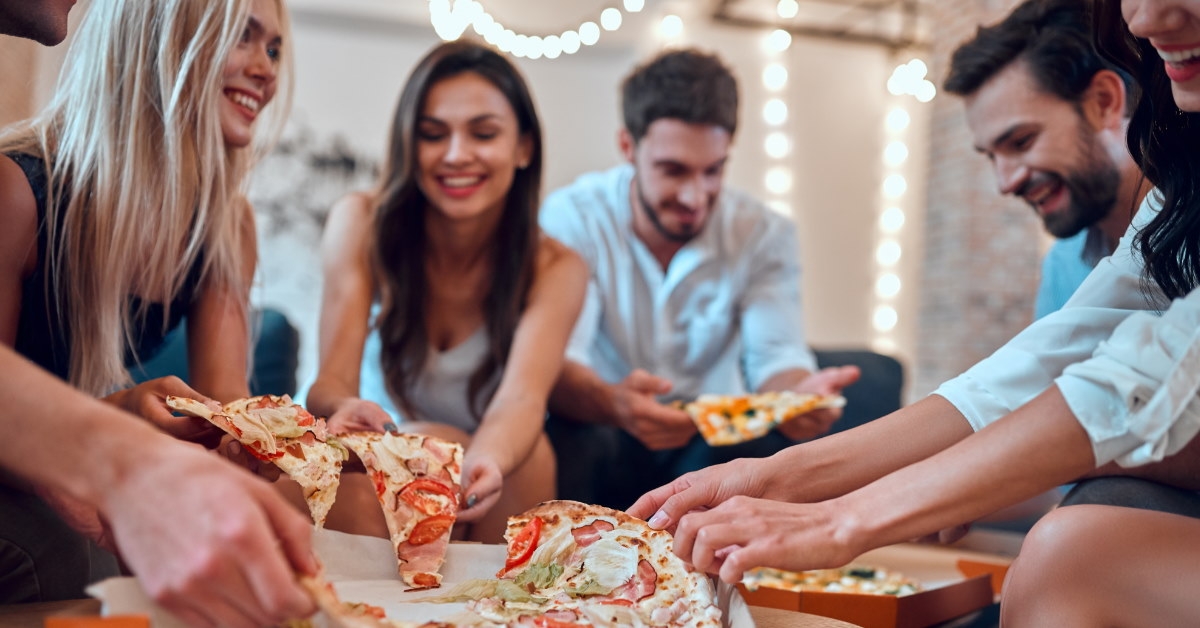 group of young friends gathered around a table eating pizza 