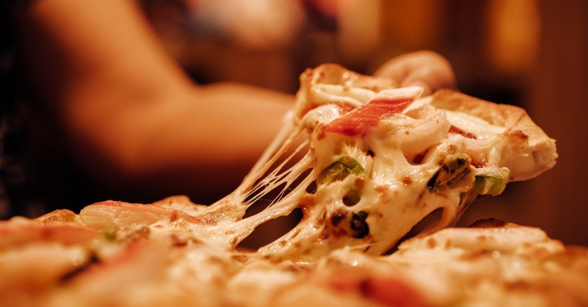 pulling apart a slice of loaded pizza with melted cheese