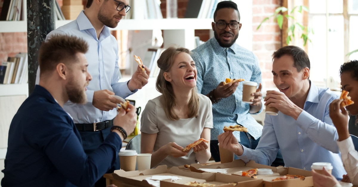 multi-ethnic colleagues chatting over pizza in office lounge.