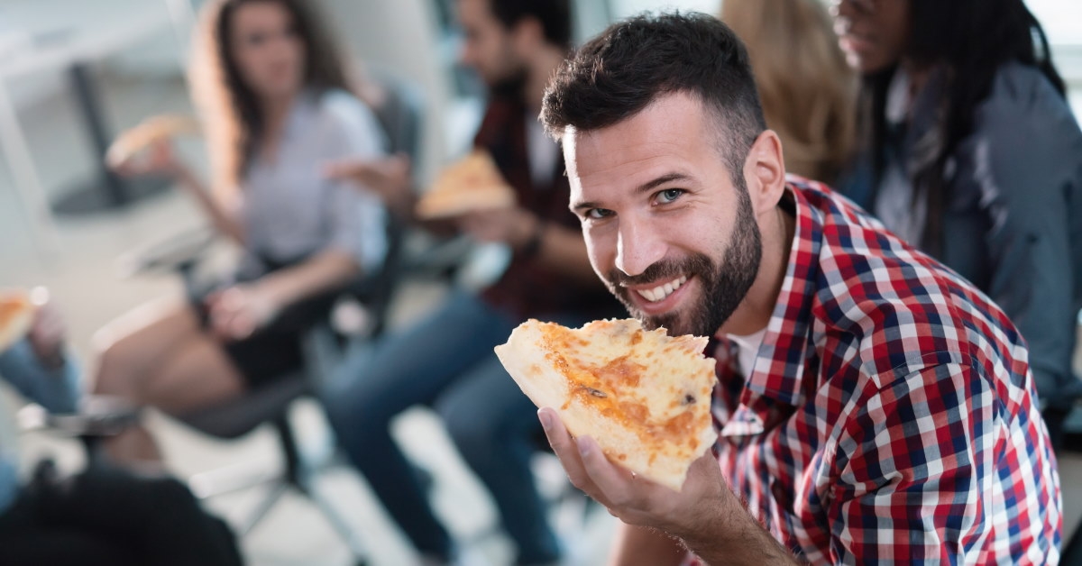 male employee enjoying pizza slice with other colleagues 