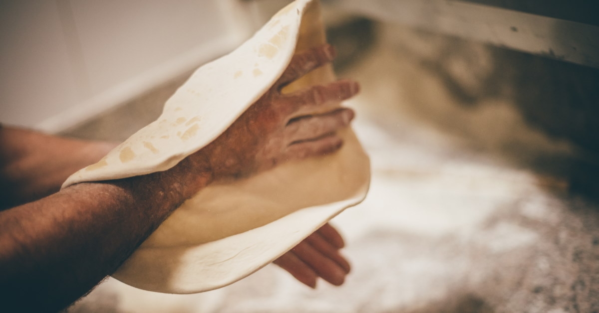 man preparing dough for pizza using hands inside professional kitchen