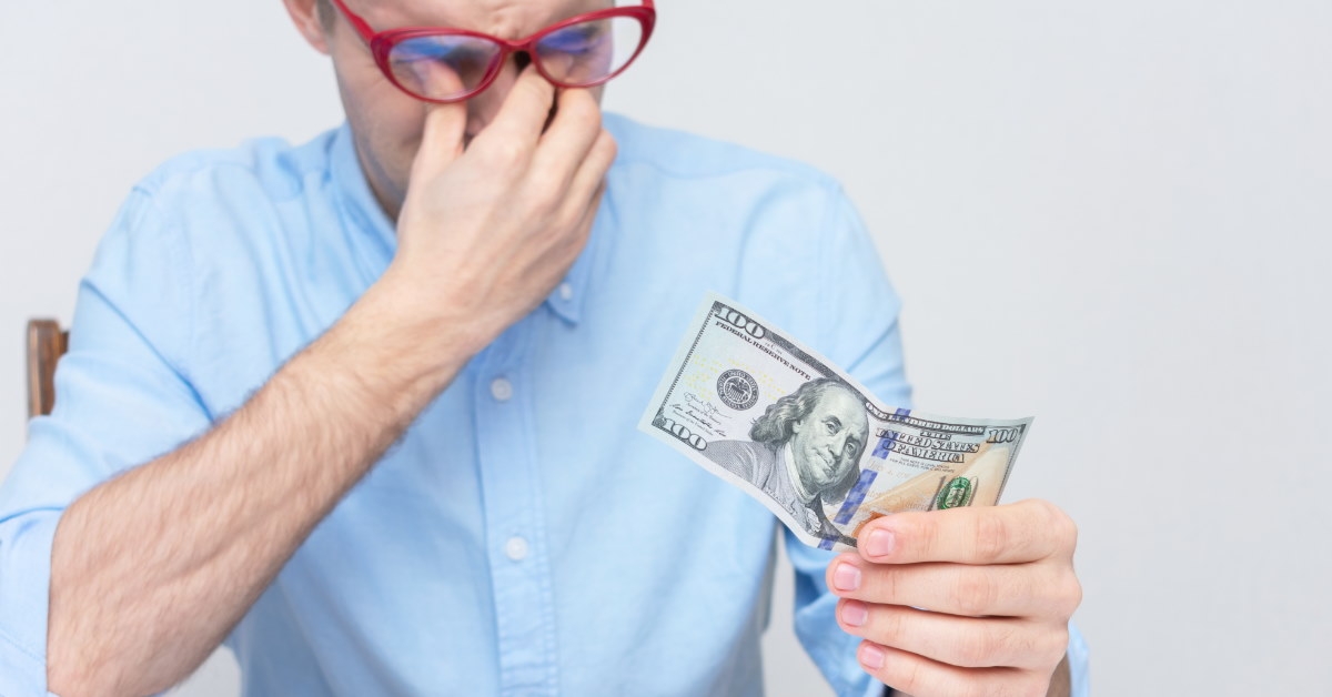 man rubbing eyes in stress holding money 