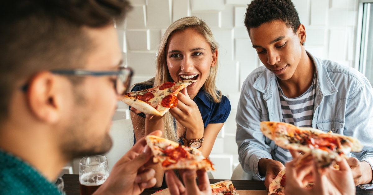 multi ethnic friends sitting in restaurent eating pizza